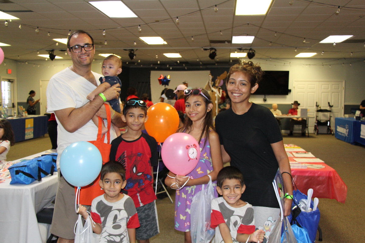 A family smiles and poses with balloons while receiving HOPE Helps Back-to-School Bash supplies.